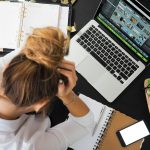 A woman is being bullied at work. She appears stressed, holding her head in frustration while sitting at her computer at her workplace.